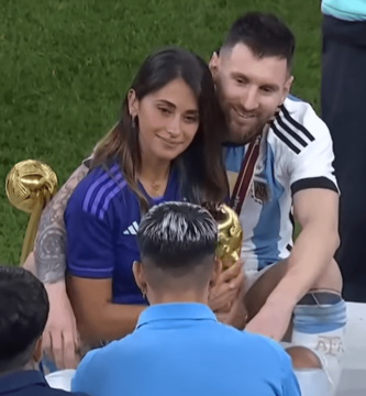 Lionel Messi abrazando a su esposa Antonela Roccuzzo mientras sostiene el trofeo de la Copa del Mundo 2022, celebrando en el campo tras la victoria de Argentina.